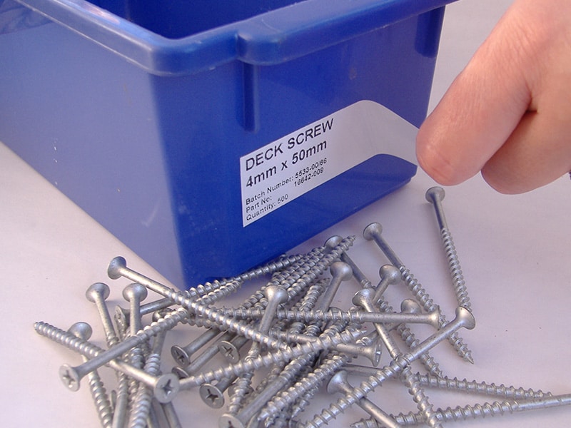 A removable label peeling away cleanly from a plastic tub of screws