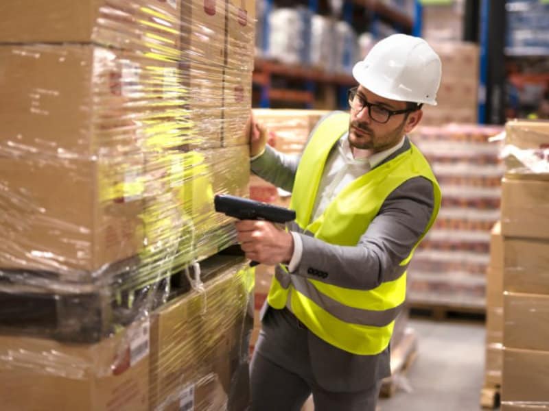 A person in a warehouse scanning pallets of goods with a handheld barcode scanner